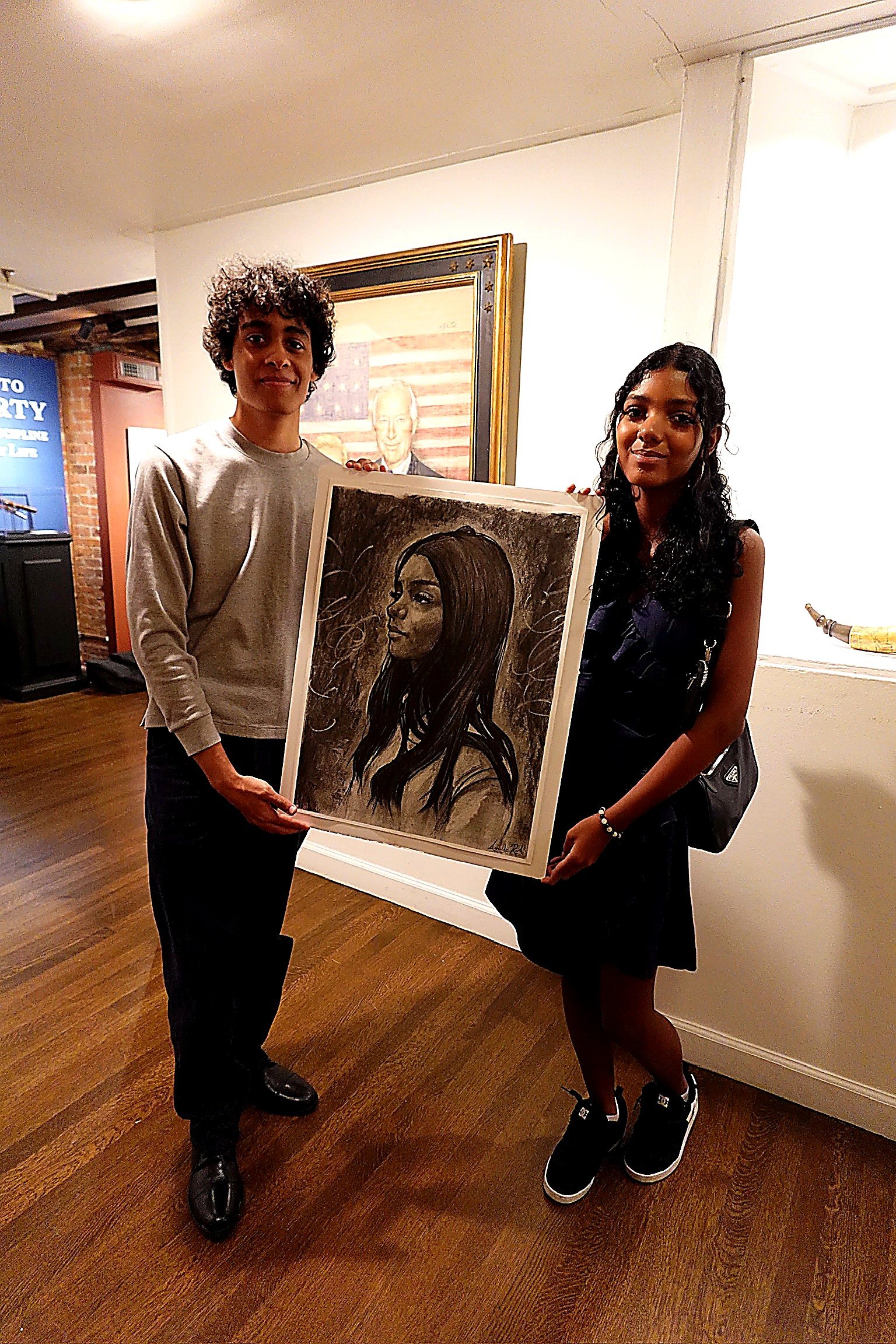 Arnaldo junto a su retrato a carboncillo y una asistente al evento.